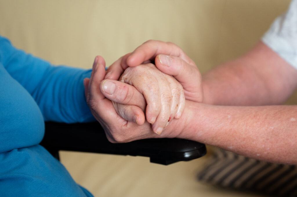 Pflegekraft hält die Hand eines älteren Menschen